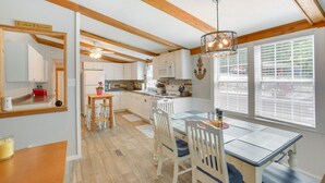 Una cocina con vigas de madera, armarios blancos, una mesa de comedor con sillas y vistas a través de las ventanas.