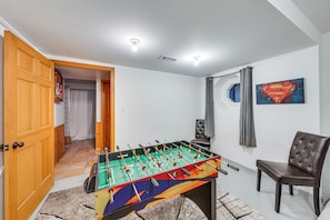 A room with a foosball table, a chair, a Superman painting, and a door leading to another room.