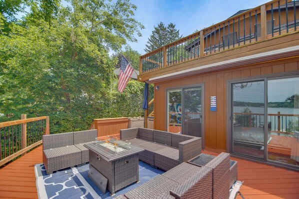 A deck with wicker furniture, a fire pit, and a view of a lake.