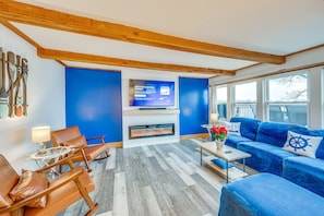 A modern living room with a fireplace, blue walls, wooden beams, leather chairs, a blue sofa, and a television screen. - Waterfront Fox Lake Vacation Rental w/ Fire Pit! (Fox Lake)