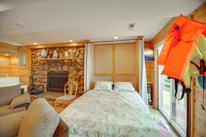 Ein gemütliches Zimmer mit Kamin aus Stein, einem Bett mit gemustertem Überwurf, einem Holzstuhl und einem Fenster mit Vorhängen.