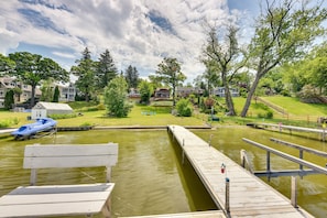 A dock with a bench, a small boat, and a grassy area with trees and houses in the background.