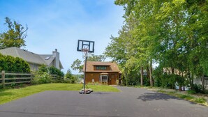 En boligkvarters indkørsel med basketballkurv, et hus og en hegnet have.
