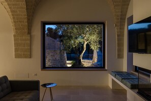 A modern living room with a large window overlooking a stone wall and tree. - Villa Trullo Cillini by Wonderful Italy (Carovigno)