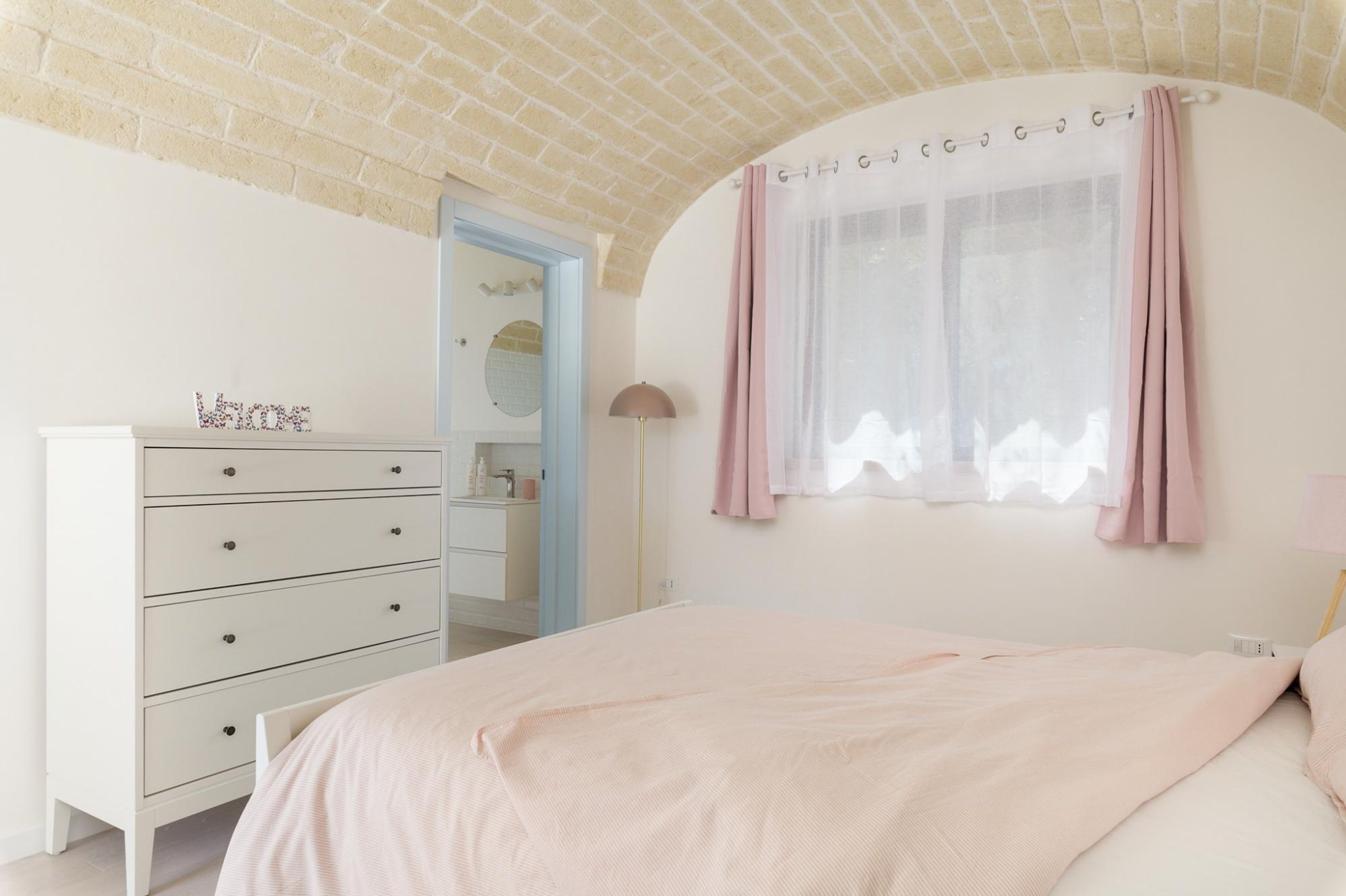 Un dormitorio con cama, cómoda, espejo y ventana con cortinas.