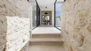 Un interior moderno con una pared de piedra, una escalera que lleva a un comedor con mesa y sillas, y un lámpara colgante.