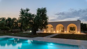 Una casa moderna con piscina, ventanas arqueadas e iluminación exterior.