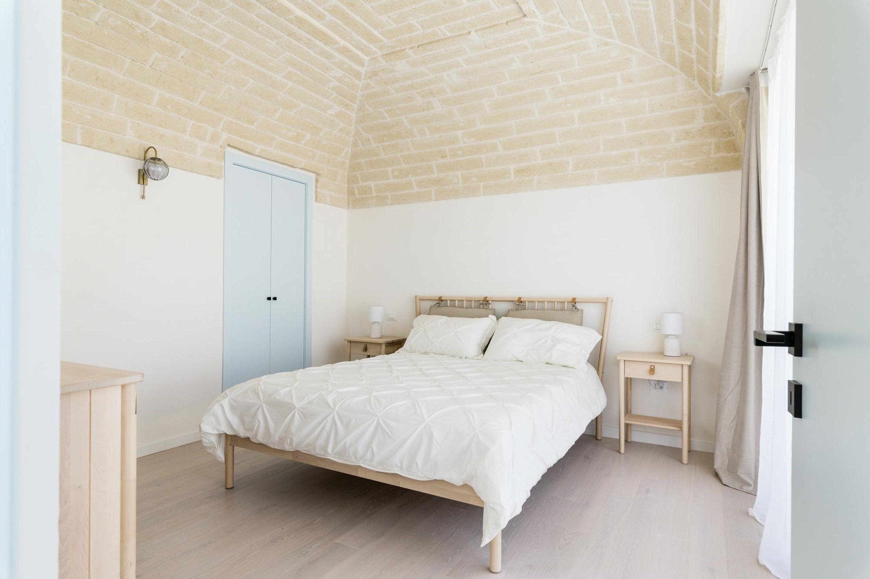 A bedroom with a wooden bed, two bedside tables, a nightstand, a door, and a brick ceiling.