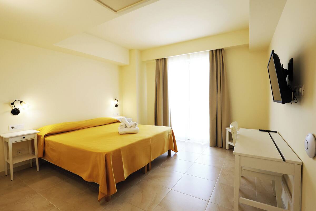 A hotel room with a bed, bedside tables, a desk, and a television.