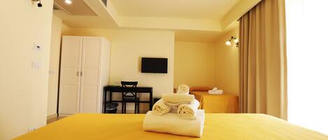 A hotel room with a bed, a desk, a chair, a TV, and a wardrobe.
