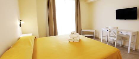 Habitación de hotel con cama, escritorio, silla, televisor y ventana con cortinas.