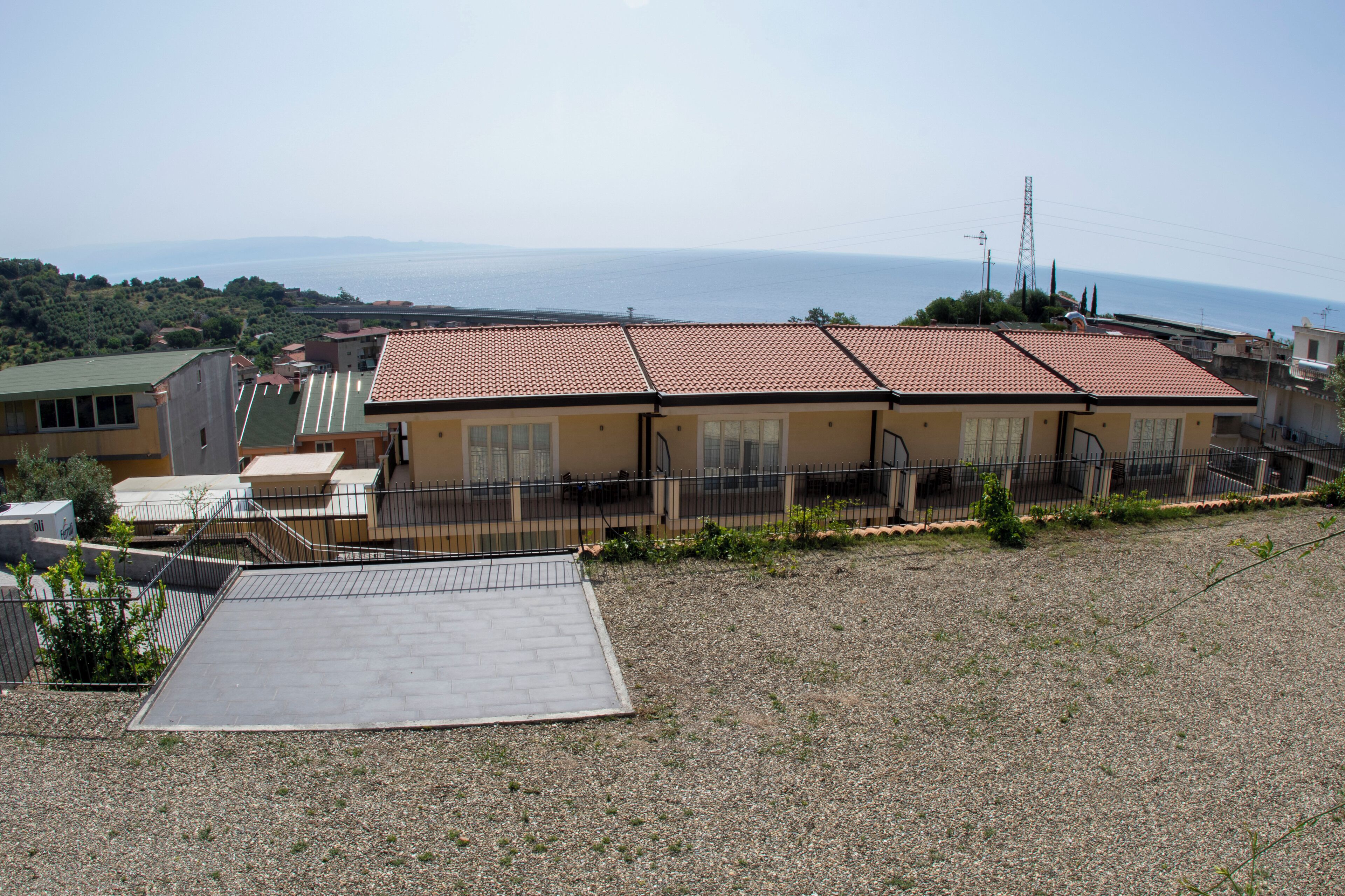 A residential building with a tiled roof, a fenced yard, and a view of the sea.