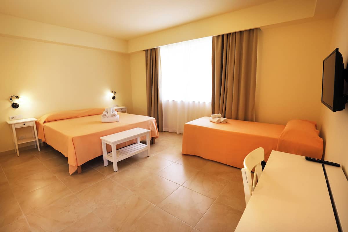 A hotel room with two beds, a desk, a chair, a TV, and a window with curtains.