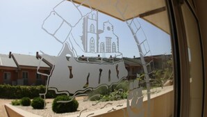 A window with a paper cut-out of a building, possibly a church, with a clear view of a building with a sloped roof in the background. - Verdello Home Savoca (Savoca)