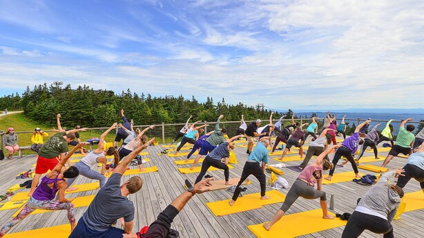 A group of people performing a yoga session outdoors on a wooden deck with a scenic view of trees and mountains in the background. - 5 minute walk to lifts and Stratton Village! Cozy fireplace with a private patio (Stratton)
