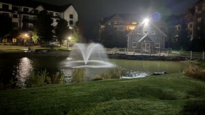 A nighttime view of a lake with a fountain, surrounded by buildings and a wooden structure labeled "Ice Skating". - 5 minute walk to lifts and Stratton Village! Cozy fireplace with a private patio (Stratton)