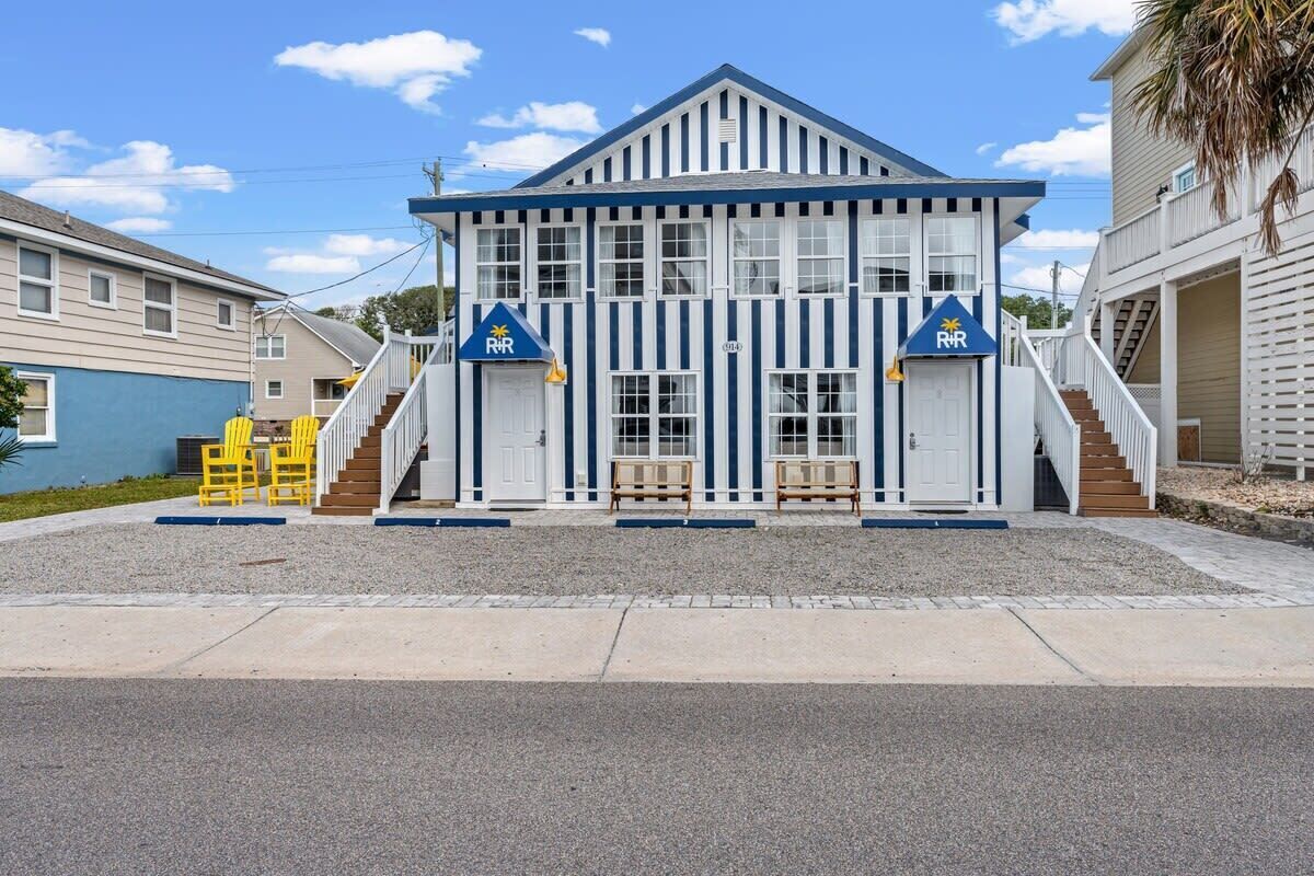 A two-story building with a white and blue striped facade, two doors marked with 'R&R', and a small outdoor seating area with yellow chairs.