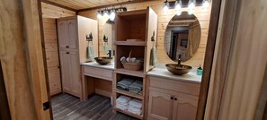 A wooden cabin-style bathroom with a sink, mirror, and shelves.
