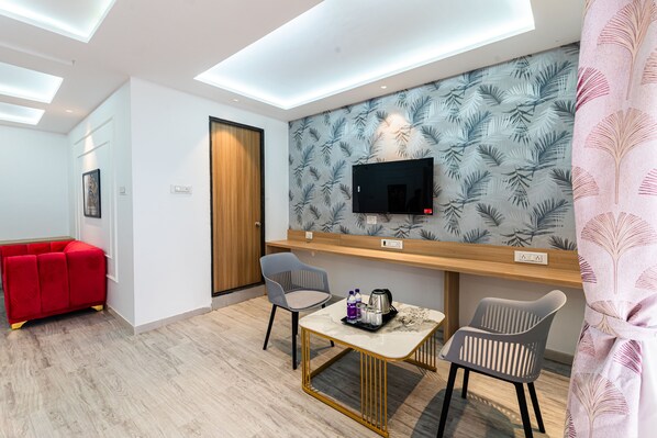Una habitación de hotel moderna con un televisor de pantalla plana montado en una pared con diseño de hojas, una puerta de madera, un sofá rojo y una mesita con una bandeja de objetos.