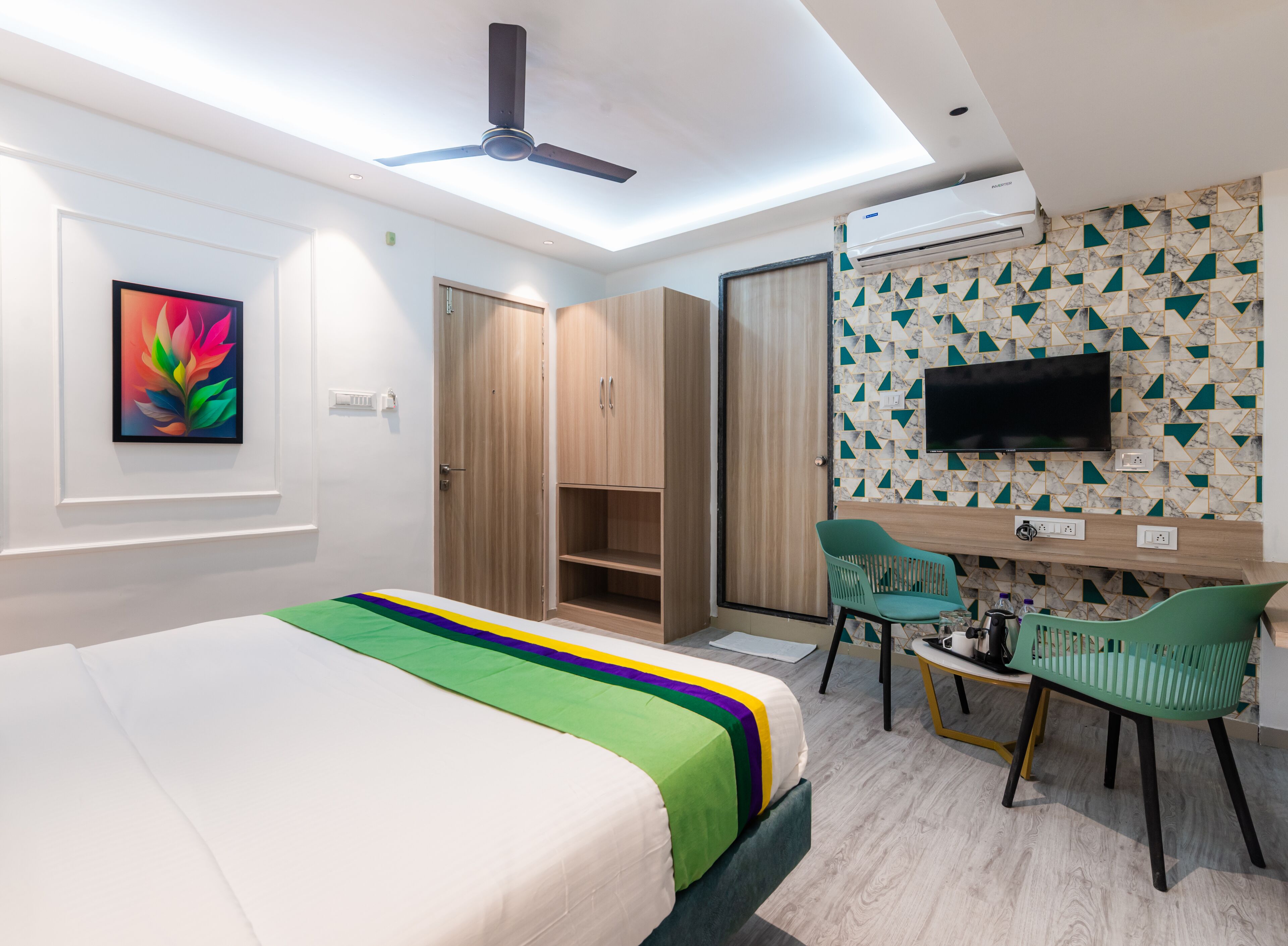 A modern hotel room with a bed, a desk, a chair, a TV, and a ceiling fan.