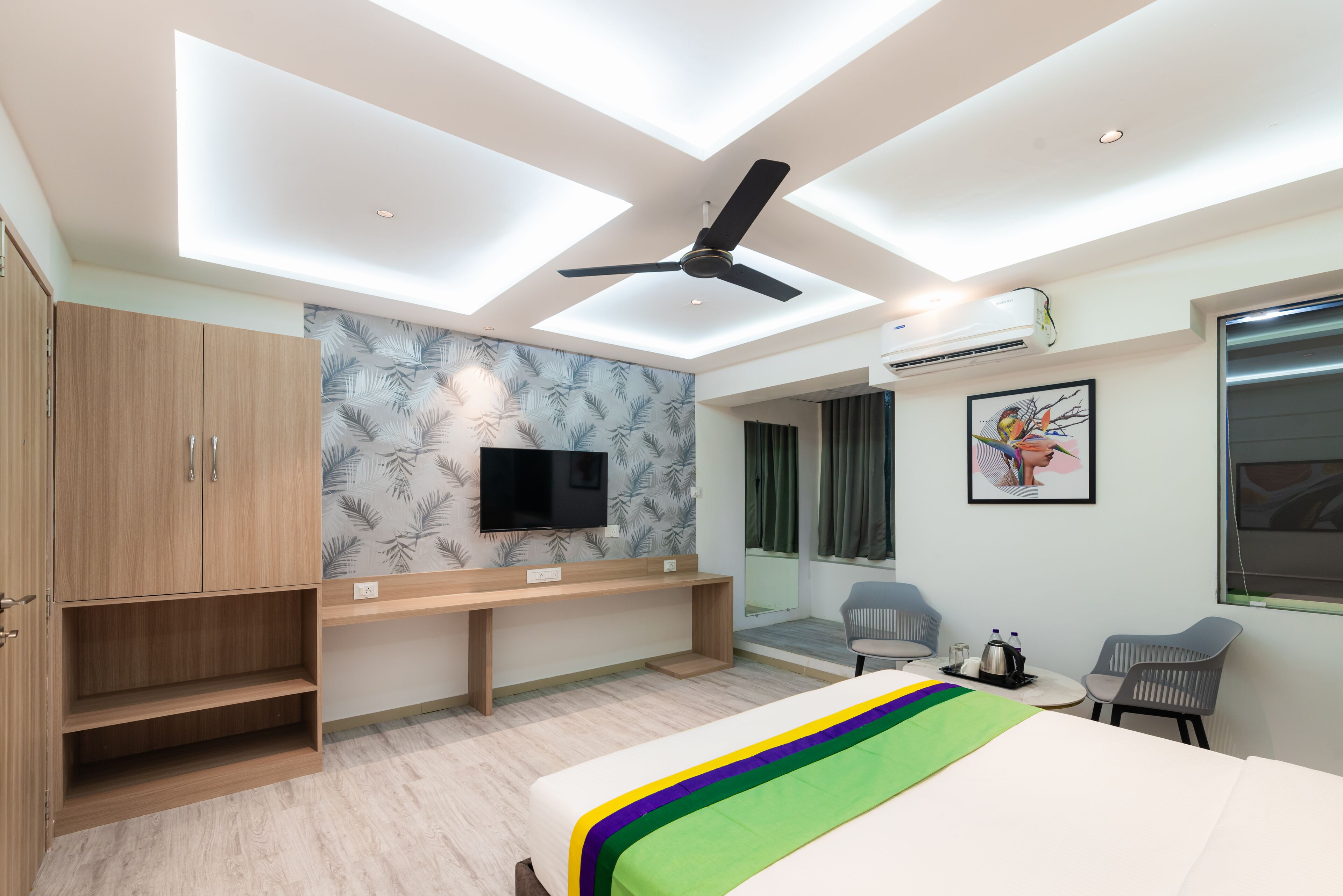 A modern hotel room with a bed, a desk, a TV, and a ceiling fan.