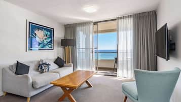 A modern hotel room with a sofa, a coffee table, a TV, and a view of the sea.