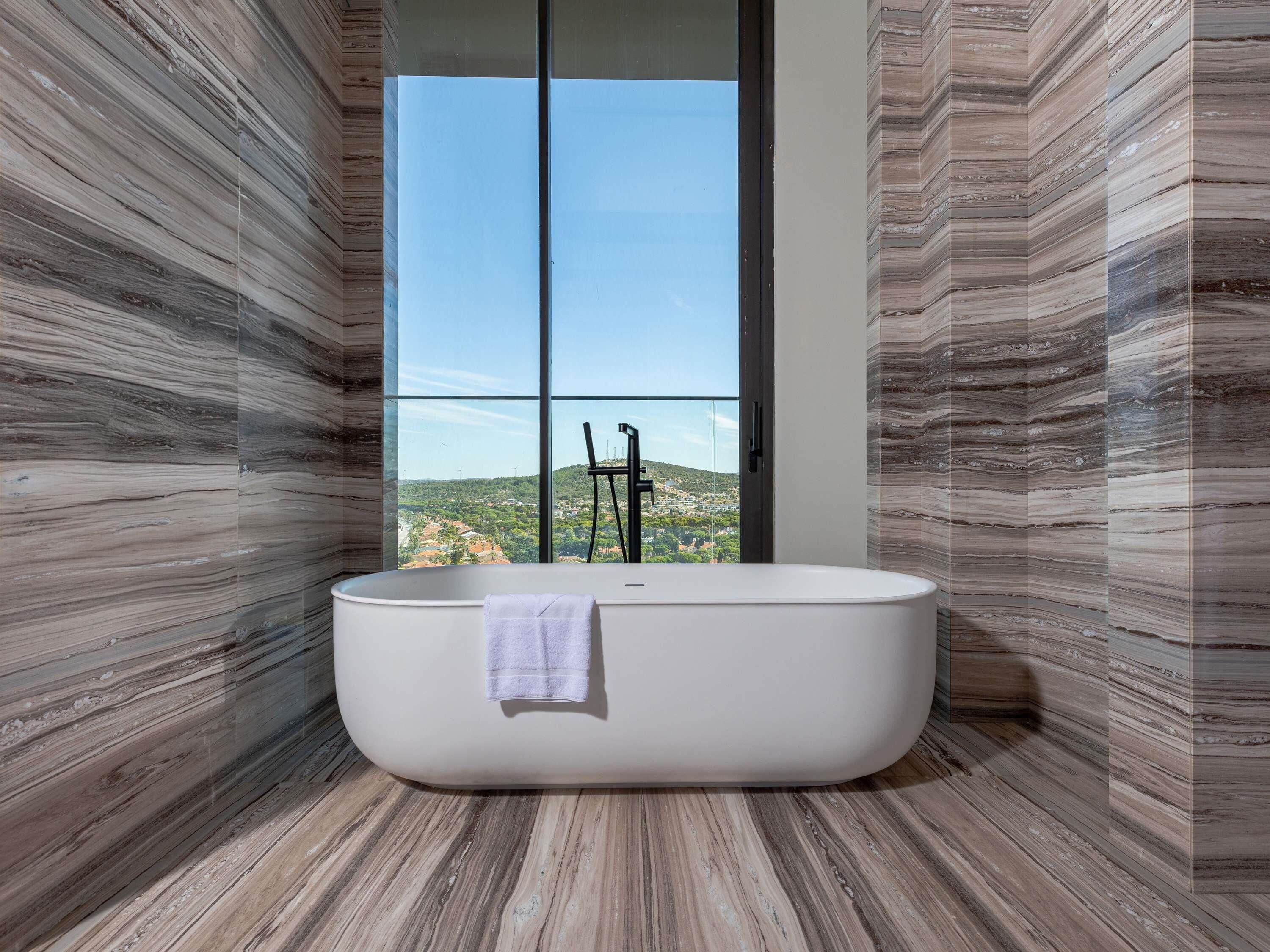 A modern bathroom with a freestanding bathtub, large windows, and a view of a mountainous landscape.