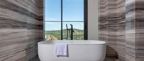 A modern bathroom with a freestanding bathtub, large windows, and a view of a mountainous landscape.