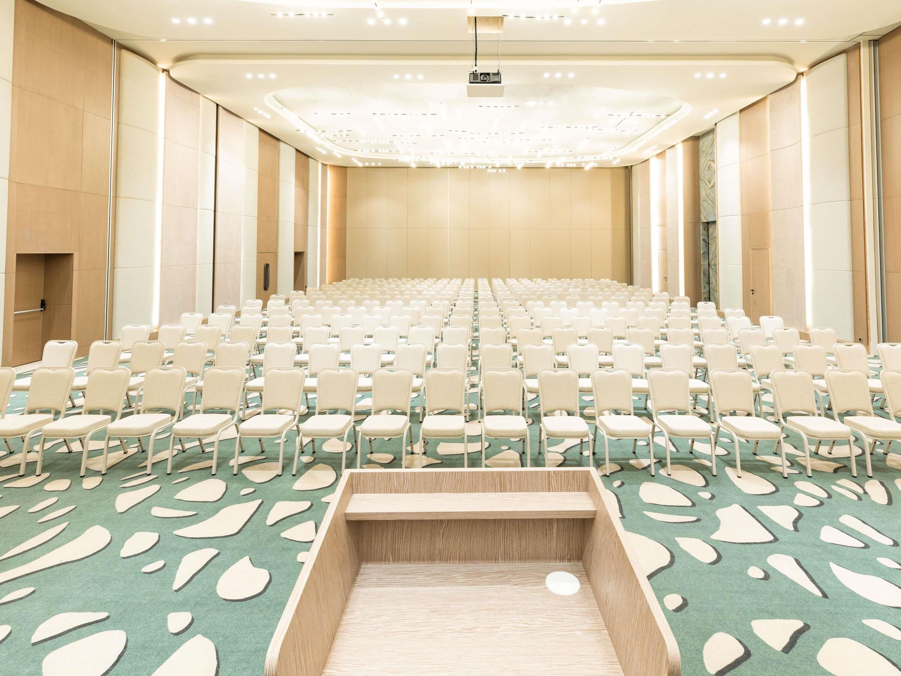 A conference room with rows of chairs, a stage, and a carpet with a leaf pattern.