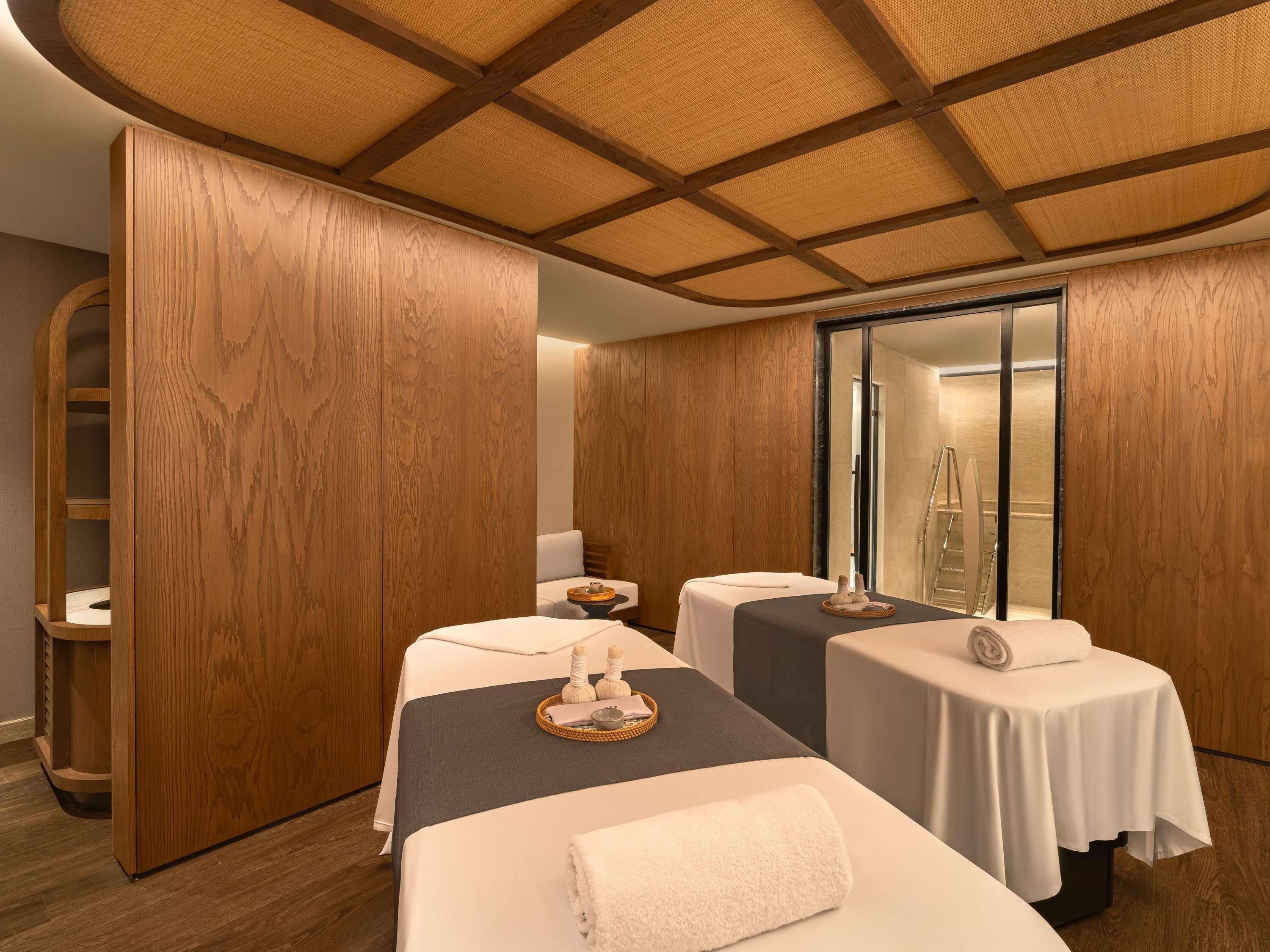 A spa room with two massage tables, wooden paneling, a large mirror, and a wooden ceiling.