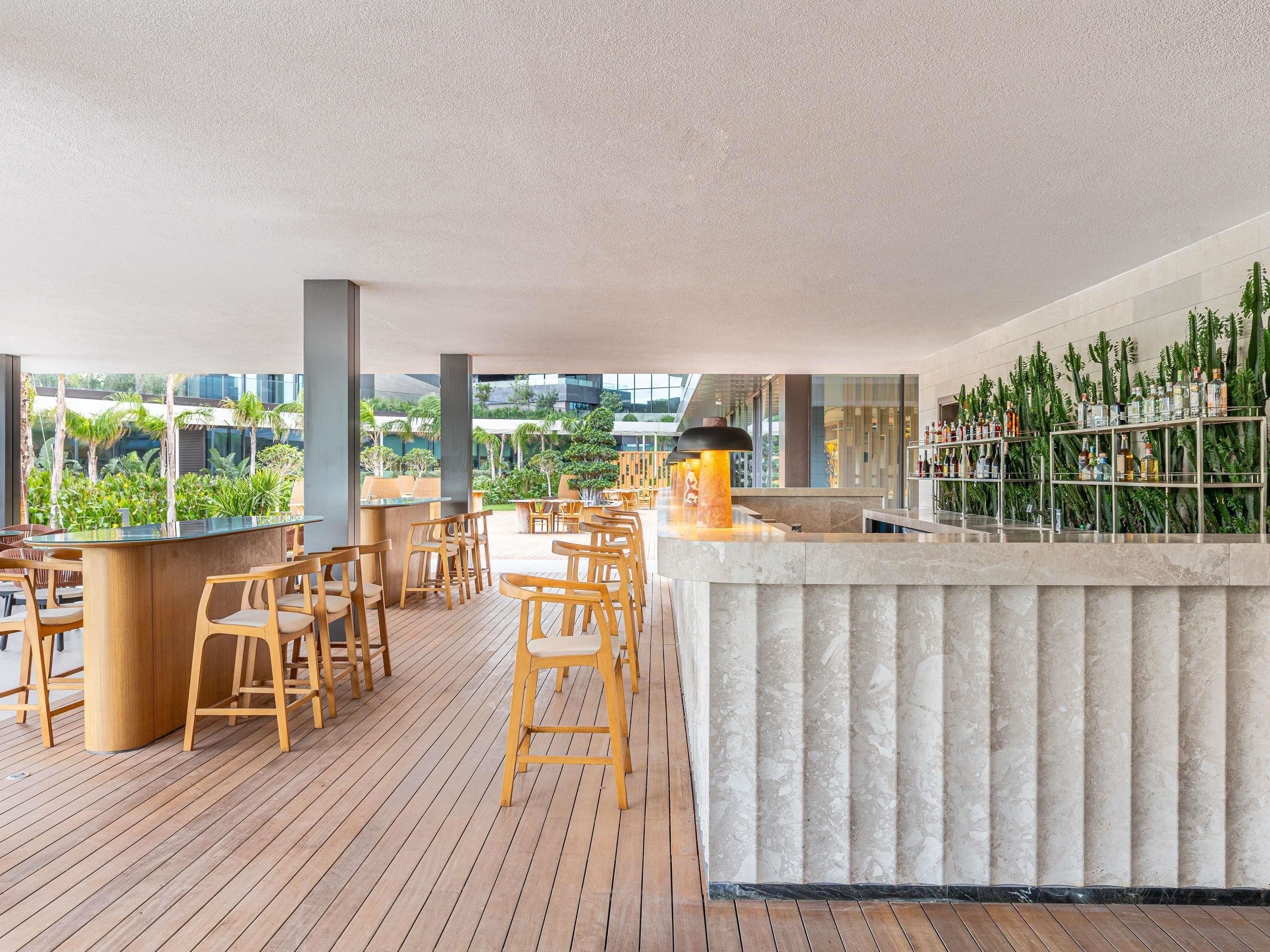 Eine Dachterrasse mit Holzstühlen, einer Bar und Blick auf Grünflächen und Gebäude.
