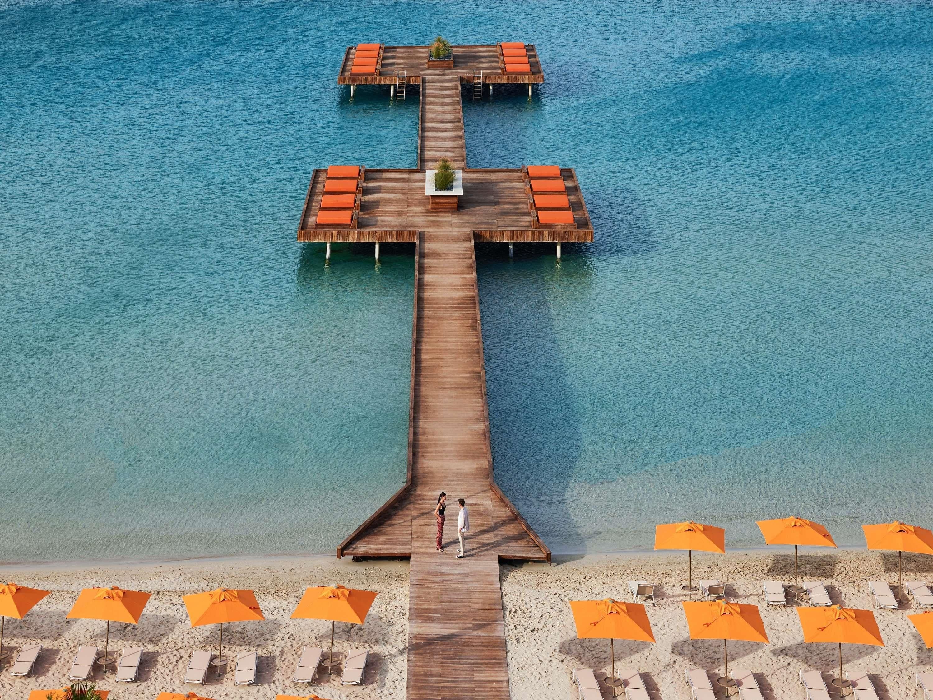 A wooden pier extending into the water with lounge chairs and umbrellas on the beach.