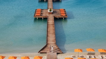A wooden pier extending into the water with lounge chairs and umbrellas on the beach.