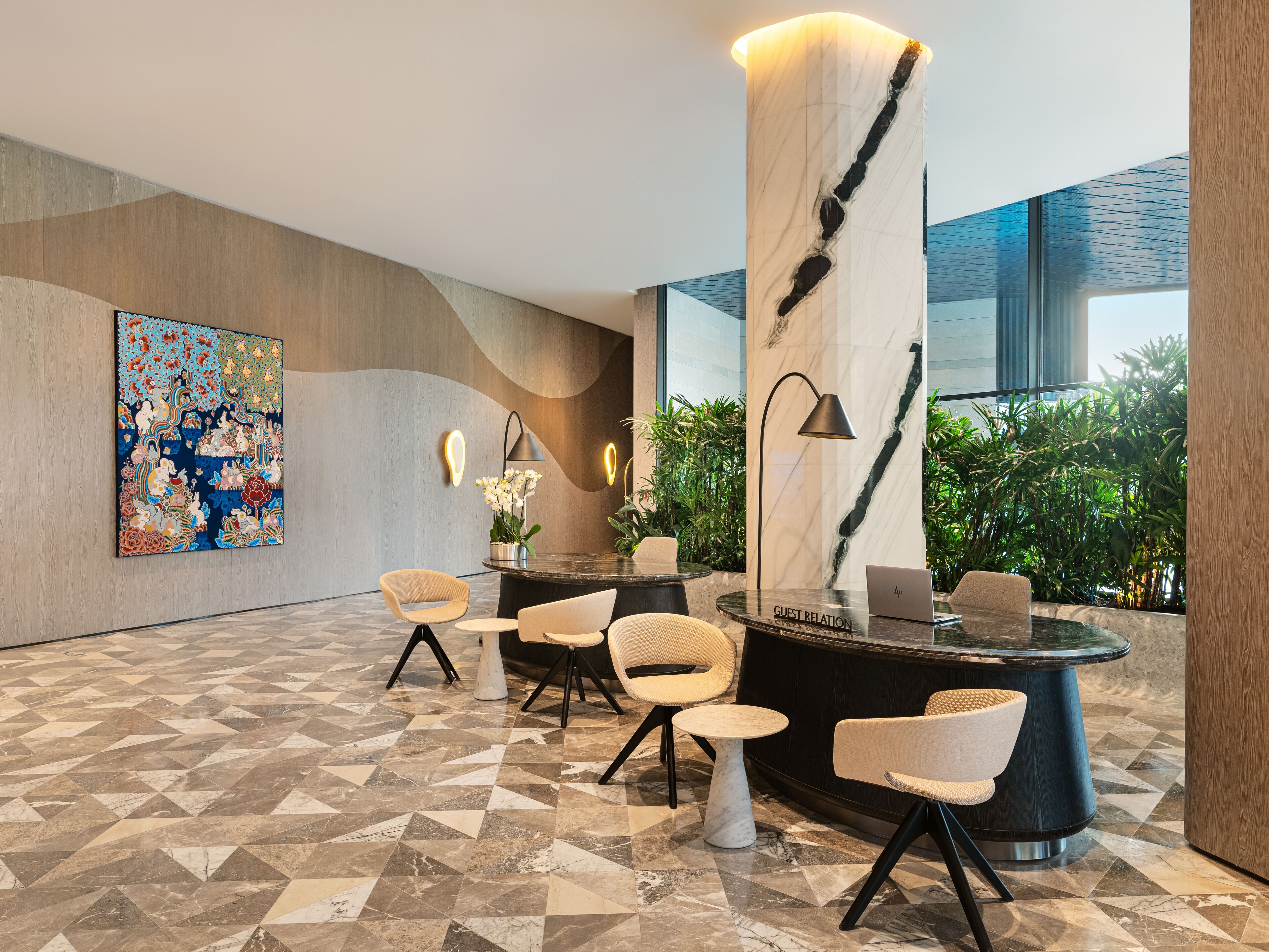 A modern lobby with a marble reception desk, comfortable seating, a large abstract painting, and a view of greenery outside.