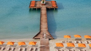 A wooden pier extending into the water with lounge chairs and umbrellas on the beach. - Swissôtel Resort And Spa Cesme (Cesme)