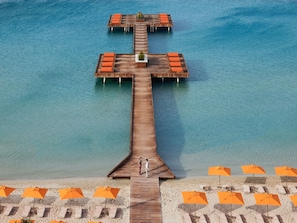 Une jetĂ©e en bois sâavançant dans lâeau, avec des chaises longues et des parasols sur la plage.