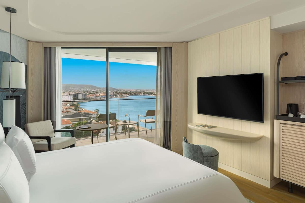 A hotel room with a large bed, a TV, a desk, and a view of a body of water.
