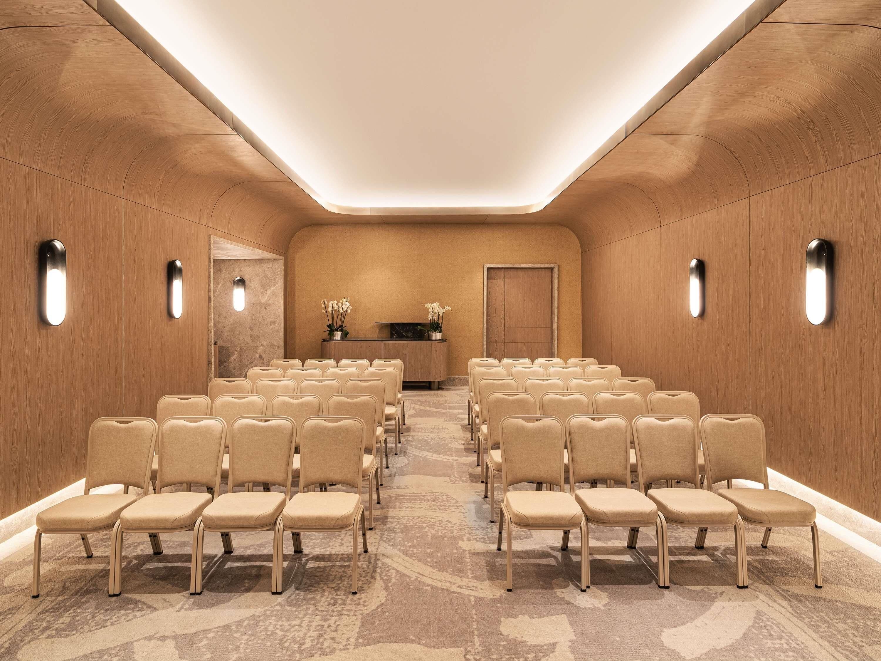 A conference room with rows of beige chairs, a reception desk, and a wooden wall with built-in lighting.