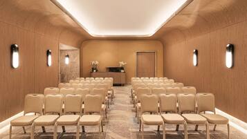 A conference room with rows of beige chairs, a reception desk, and a wooden wall with built-in lighting.