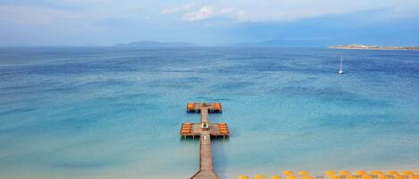 A beach view with a wooden pier leading to a sandy area with sun loungers and umbrellas.