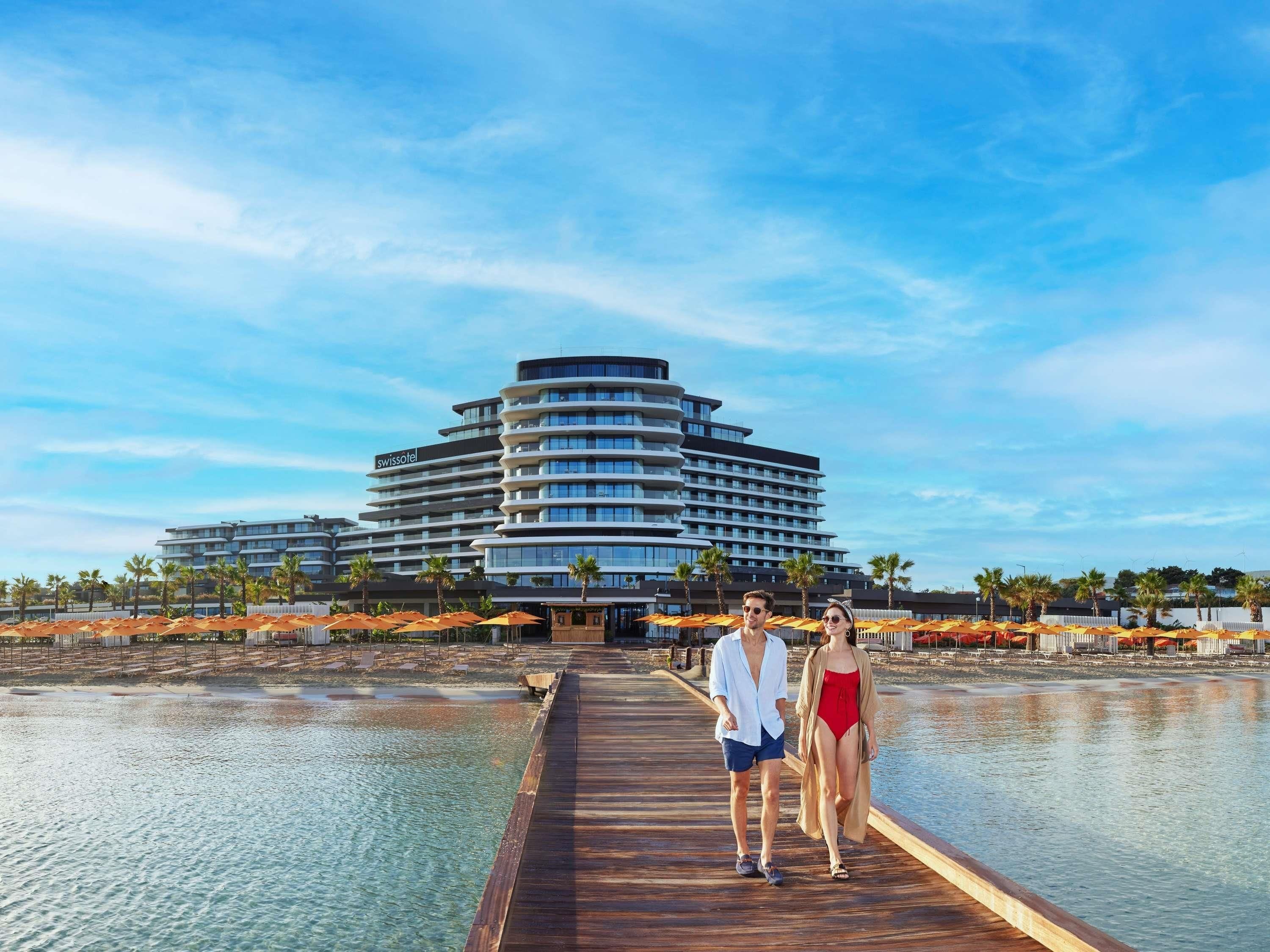 Un hôtel moderne doté d’un bâtiment aux lignes courbes, d’une jetée en bois et bordant un plan d’eau paisible.