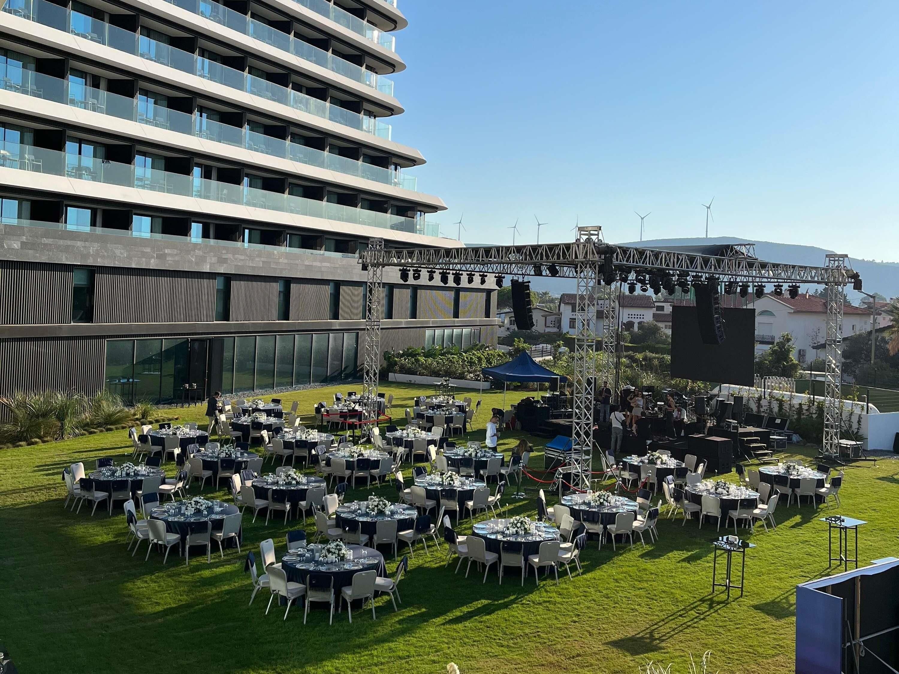 A rooftop dining area with multiple tables and chairs, a stage with lighting equipment, and a modern building in the background.