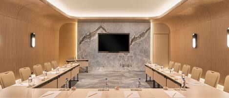 Un salón de conferencias con una larga mesa, sillas, un televisor de pantalla plana y una pared de mármol.