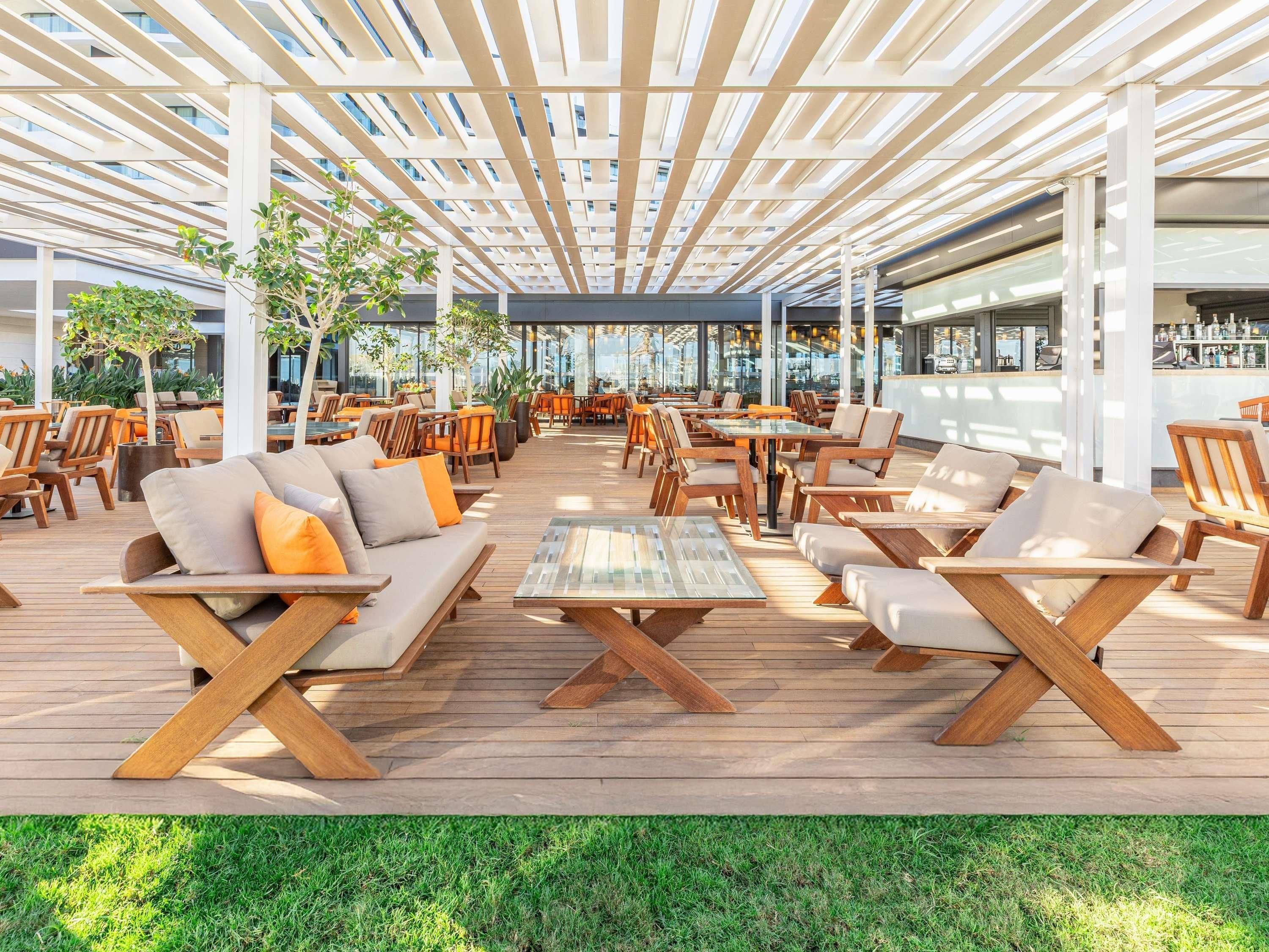 Een terras buiten met houten meubels, een glazen bijzettafeltje en een overdekt gedeelte met uitzicht op de stad.