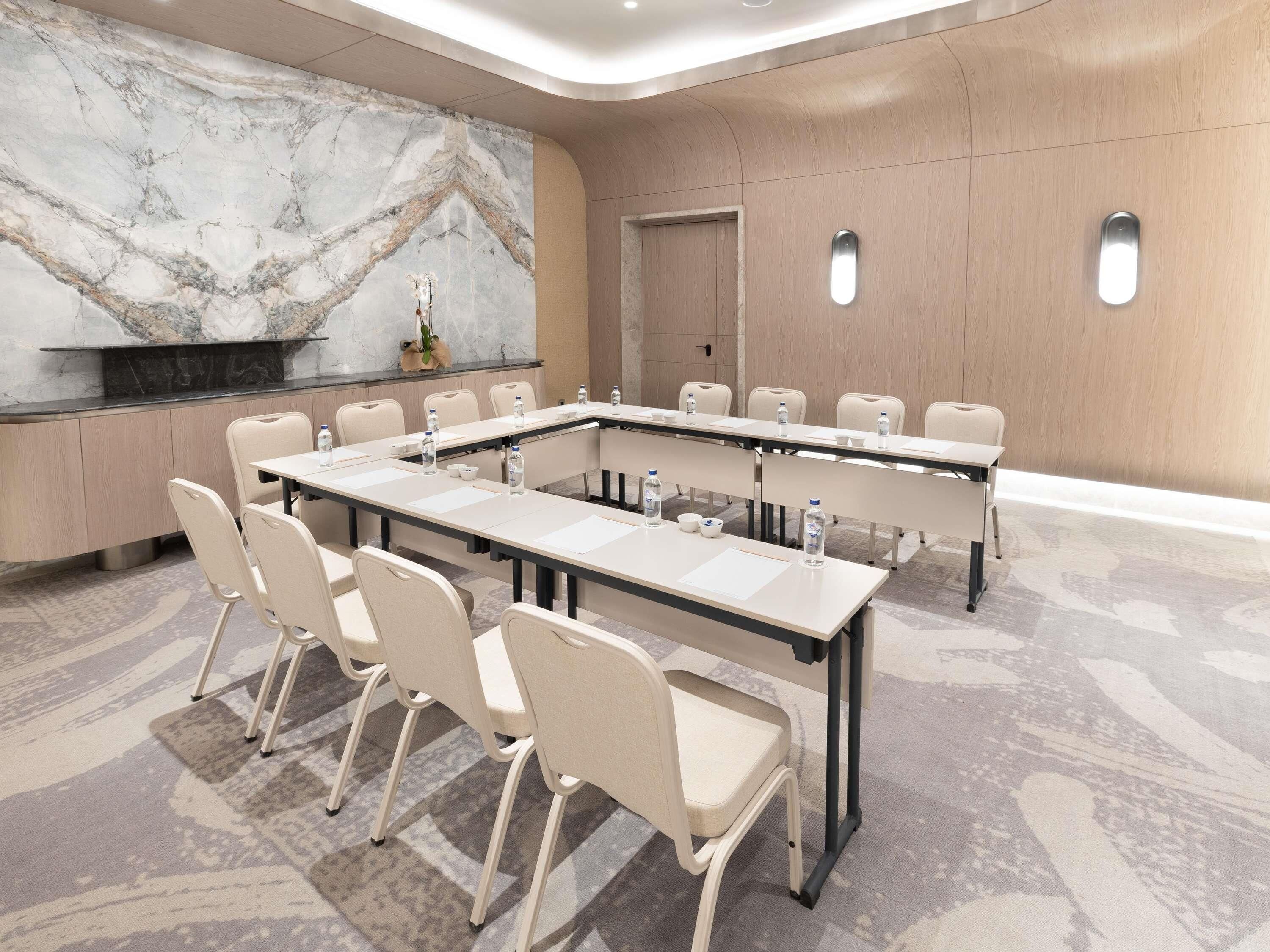 Un salón de conferencias con pared de mármol, una mesa larga con sillas y una puerta al fondo.