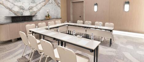 Un salón de conferencias con pared de mármol, una mesa larga con sillas y una puerta al fondo.
