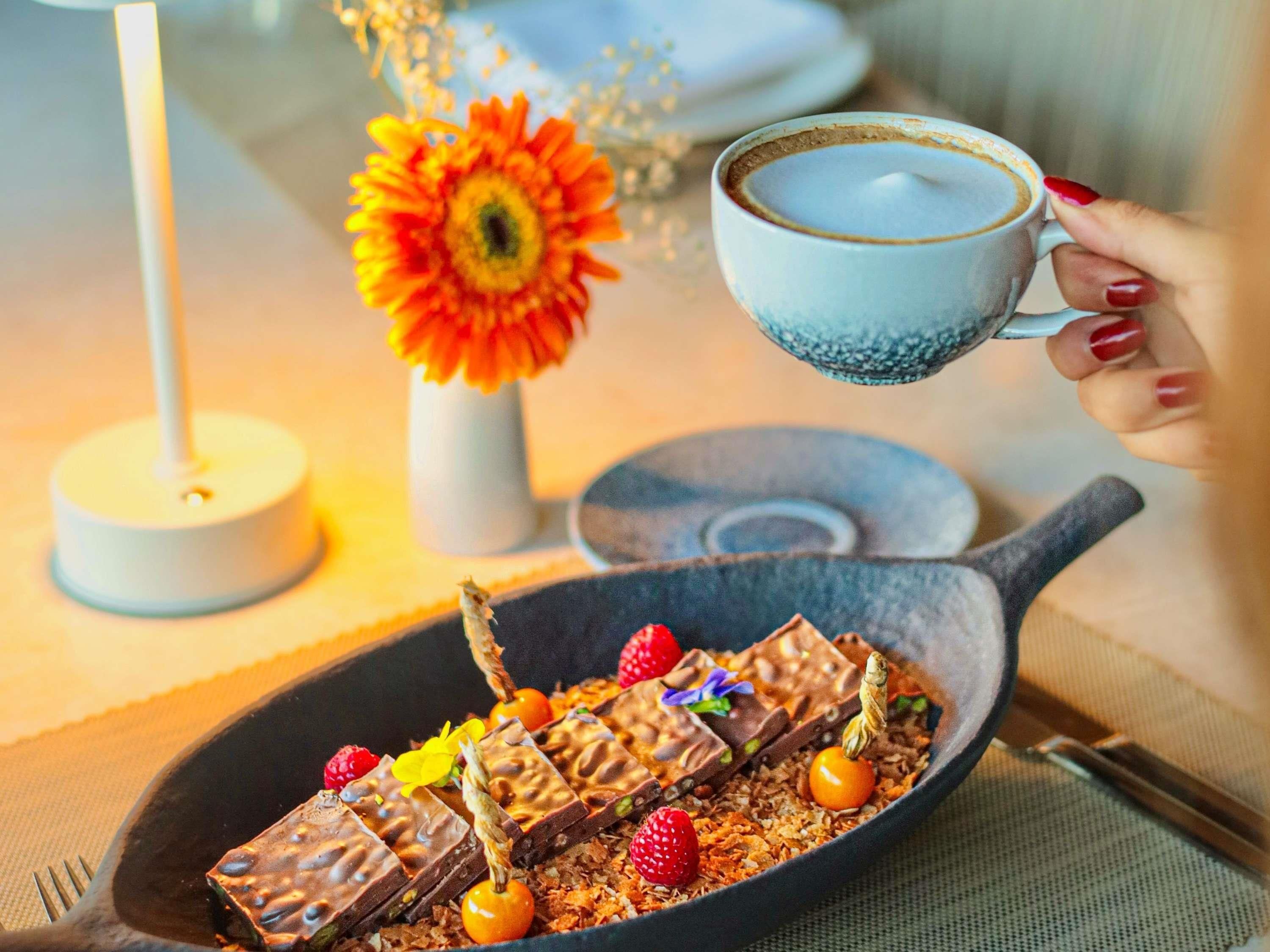 A dessert plate with chocolate bars, strawberries, and a flower, and a hand holding a cup.