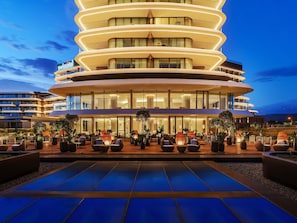 Un hotel moderno con fachada curva, asientos exteriores y zona de piscina.