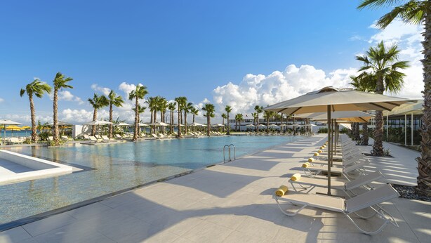 A pool area with lounge chairs and umbrellas, surrounded by palm trees. - Swissôtel Resort And Spa Cesme (Cesme)