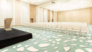 A conference room with rows of white chairs, a stage with a podium, and a patterned carpet.